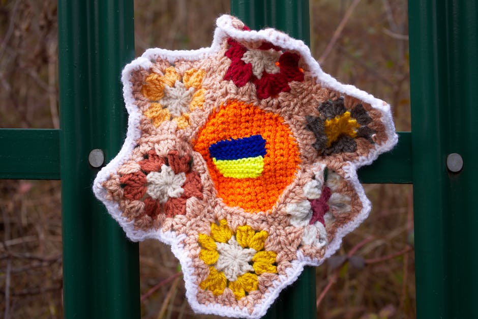 Bright crocheted floral piece displayed on a green fence showcasing handmade textile flowers