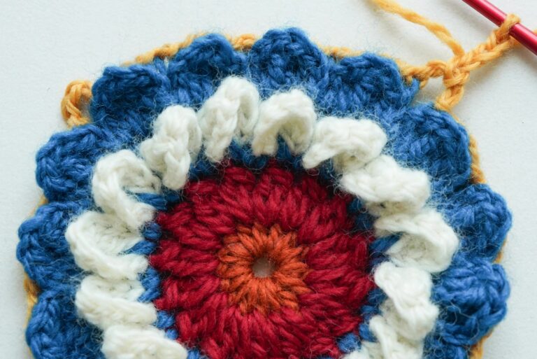 Folk flower medallion granny square with layered white petals creating 3D texture on colorful background