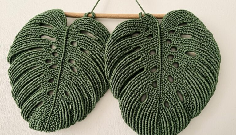 monstera crochet pattern - Handcrafted crochet monstera leaf wall hanging made of green yarn with realistic Swiss cheese plant leaf shape displayed on white wall with wooden dowel.