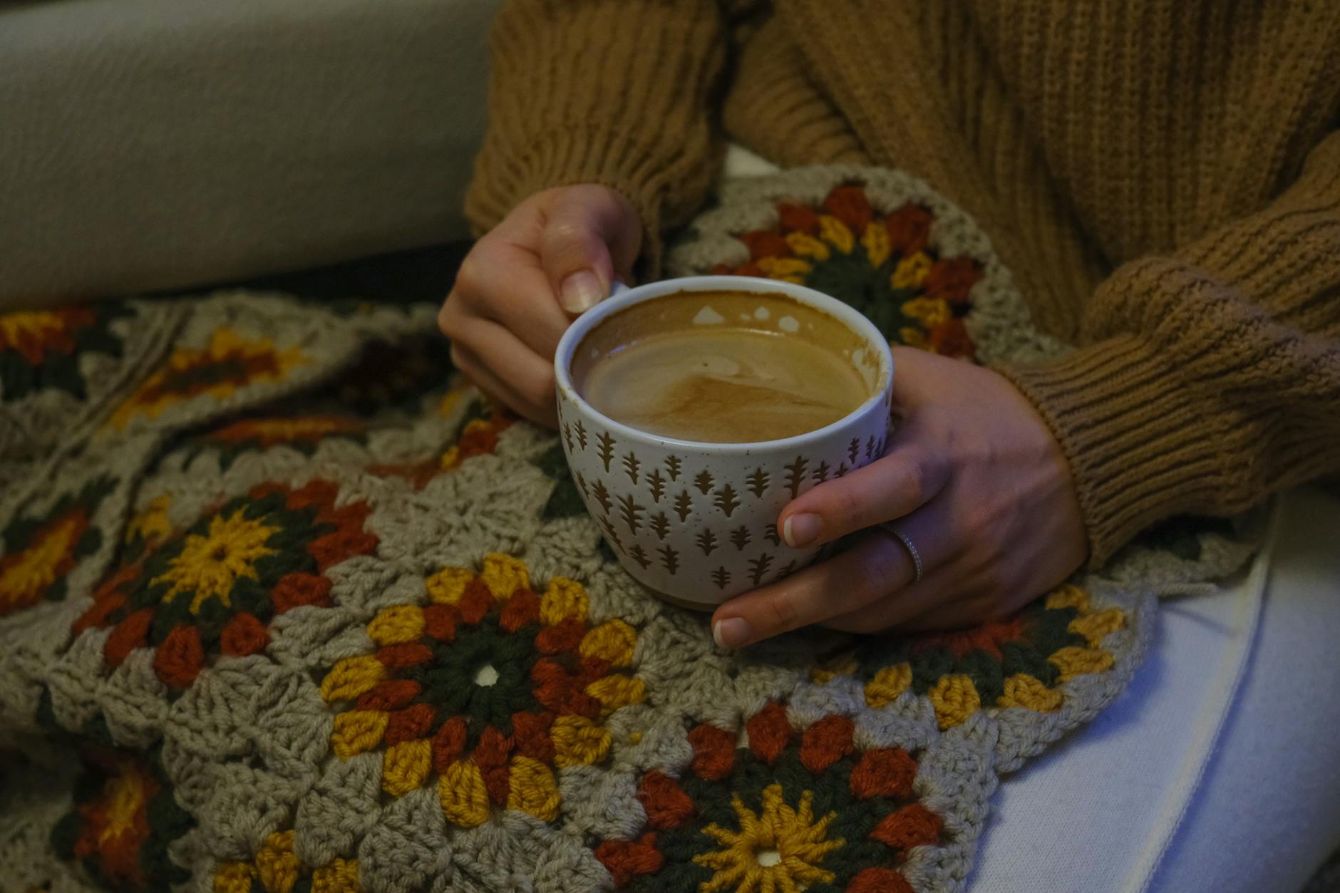 granny square blanket pattern - A person holding a warm coffee cup wrapped in a handmade crochet blanket, creating a cozy ...