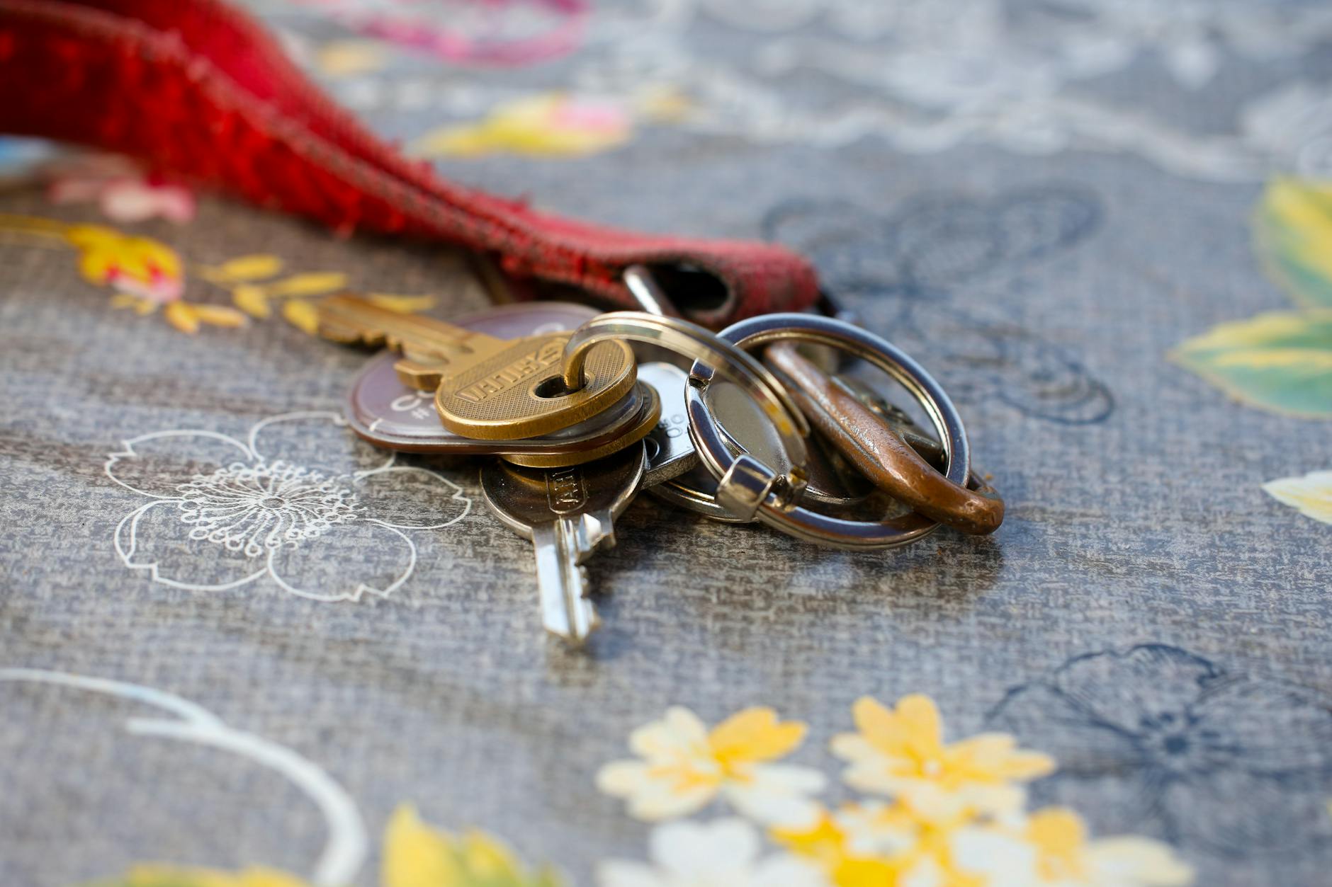 crochet keychain patterns - A set of keys lying on a floral-patterned fabric background. Ideal for security themes.