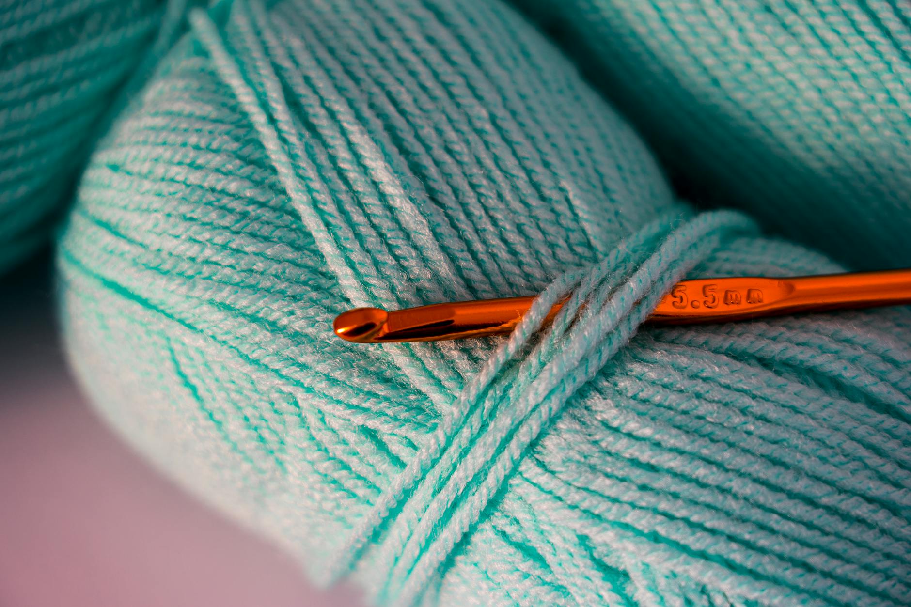 granny square cardigan patterns - Macro photograph of teal yarn with a crochet hook, highlighting texture and detail.