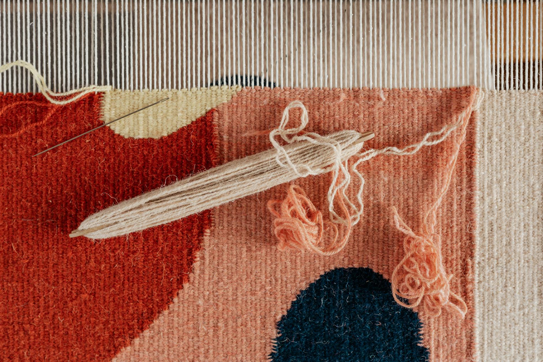 weaving in ends - From above of shuttle and needle placed on part of handmade carpet with circle pattern on l