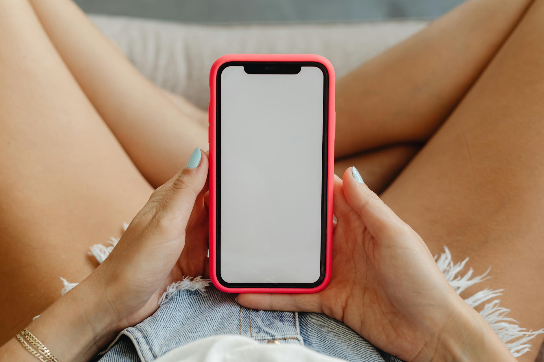 crochet phone case pattern guide - Close-up of a woman holding a smartphone in denim shorts, showcasing the phone display.