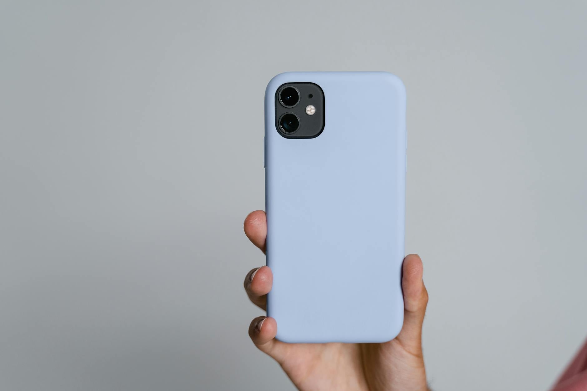 crochet phone case pattern guide - A person holding a smartphone with a light blue case against a plain white background.