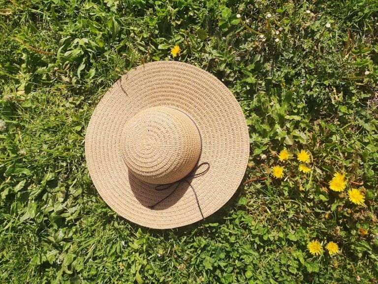 Crochet sun hat pattern inspiration - wide brimmed straw hat resting on a grassy field with yellow flowers under sunlight