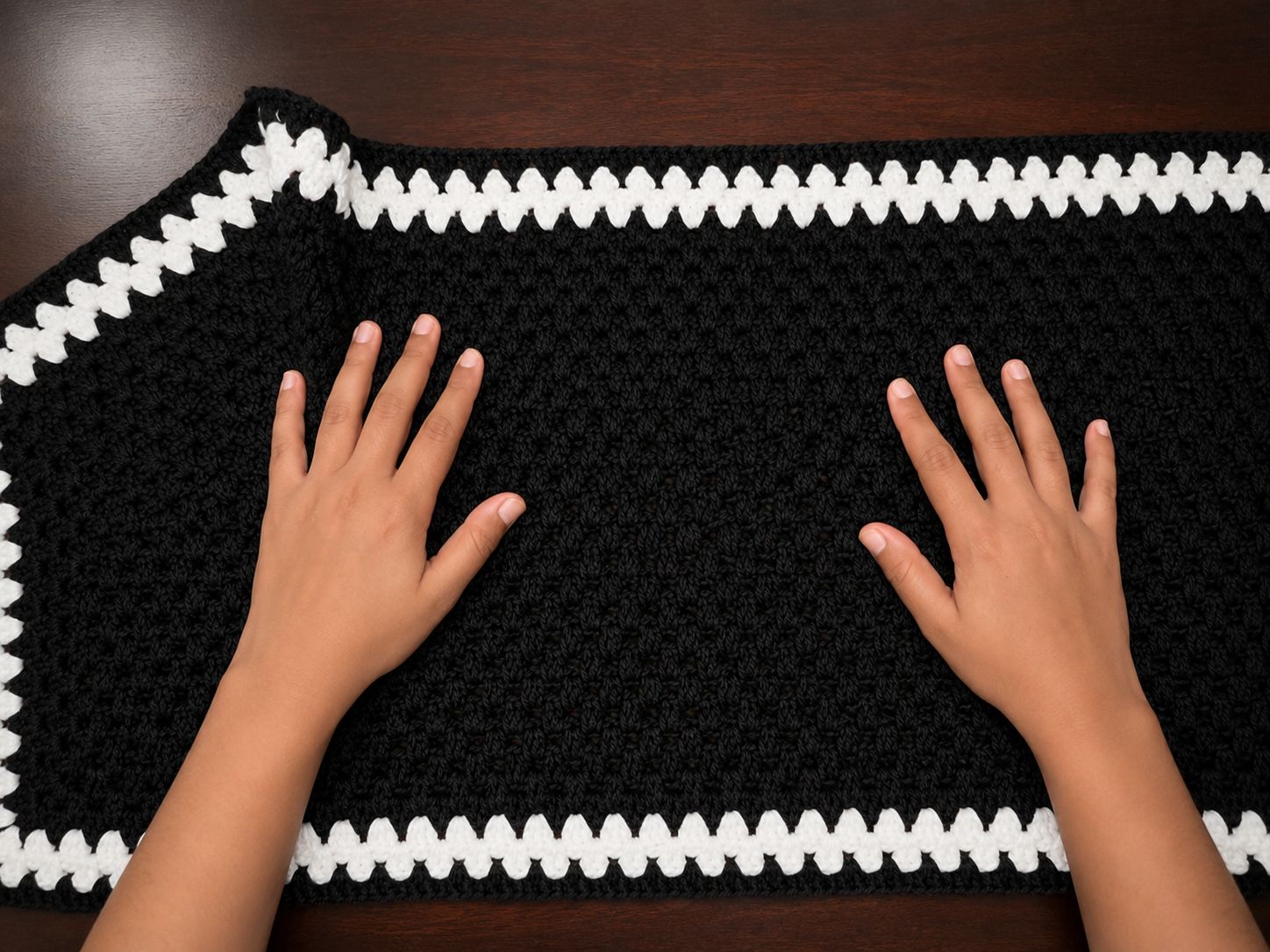 Positioning a black crocheted hexagon panel with white border for shirt assembly