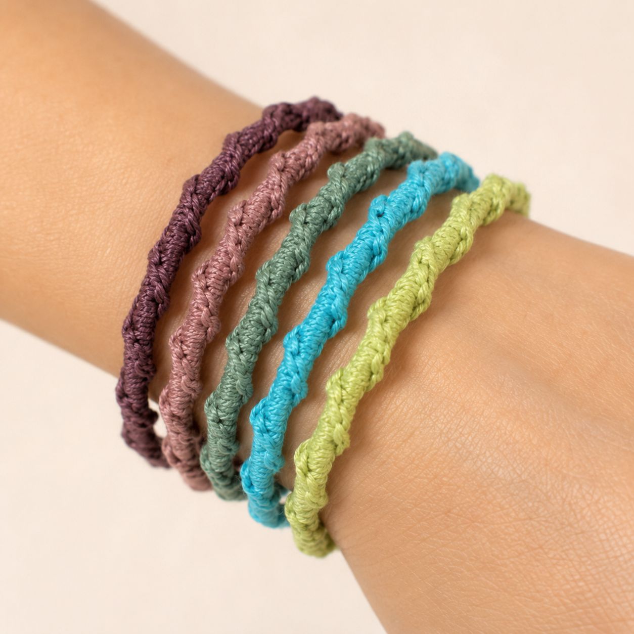 Five thin twisted stitch crochet bangles in purple mauve teal turquoise and lime green stacked on wrist