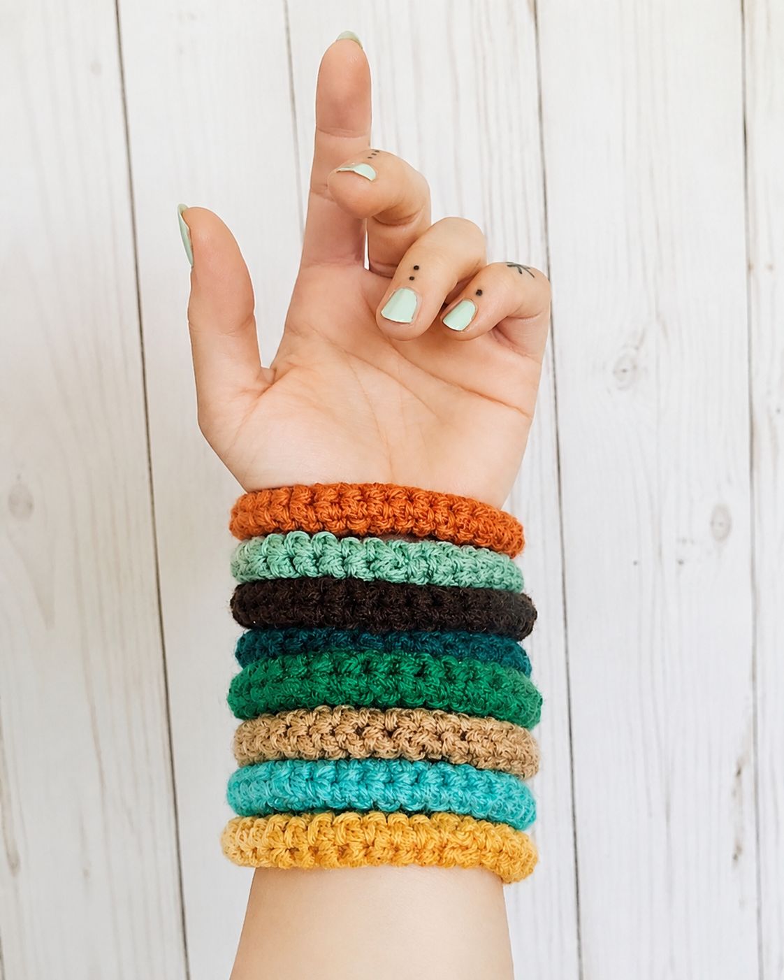 Seven stacked crochet bangle bracelets in orange mint black teal green tan turquoise and yellow