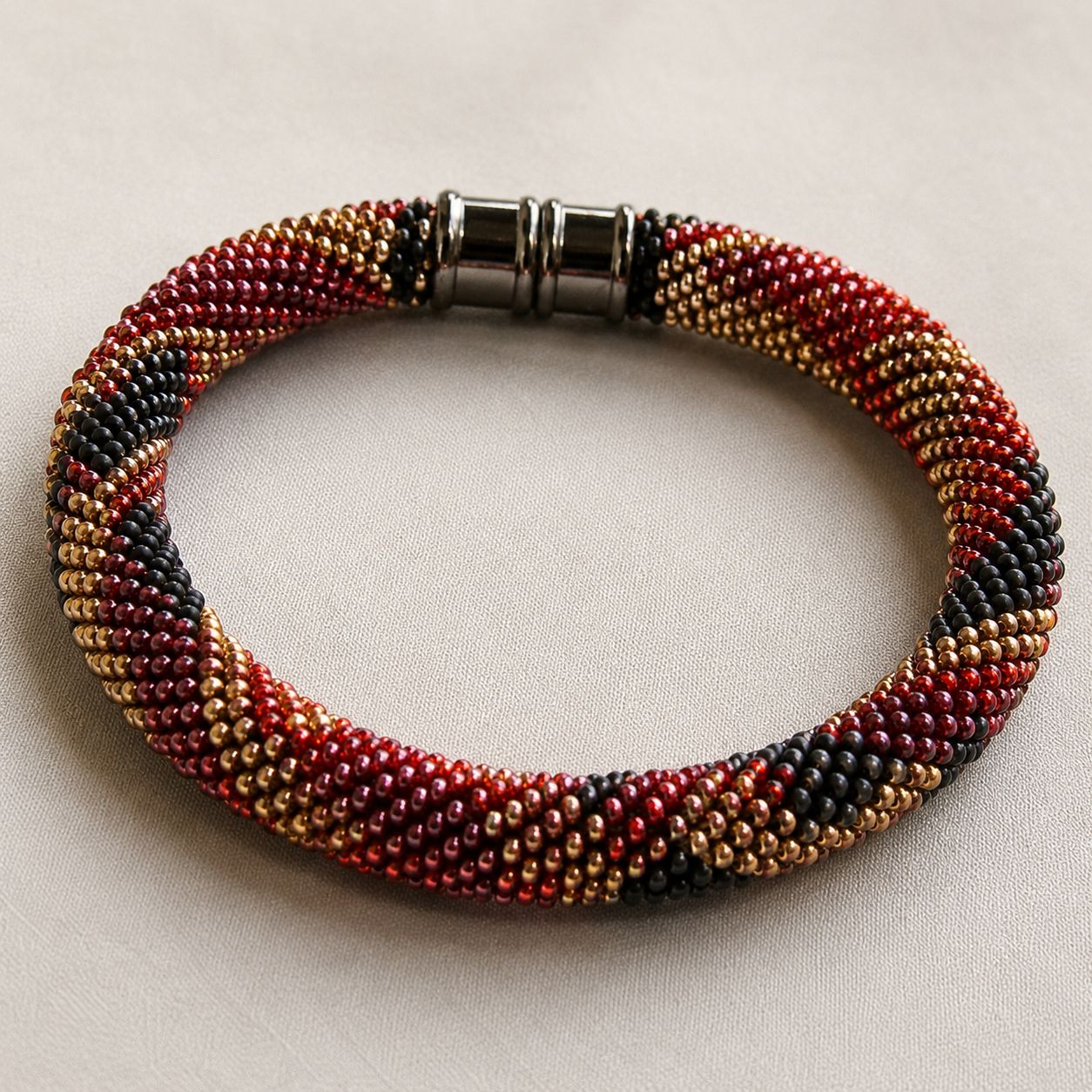 Single beaded crochet bangle with red gold and black beads featuring twisted design and metal clasp