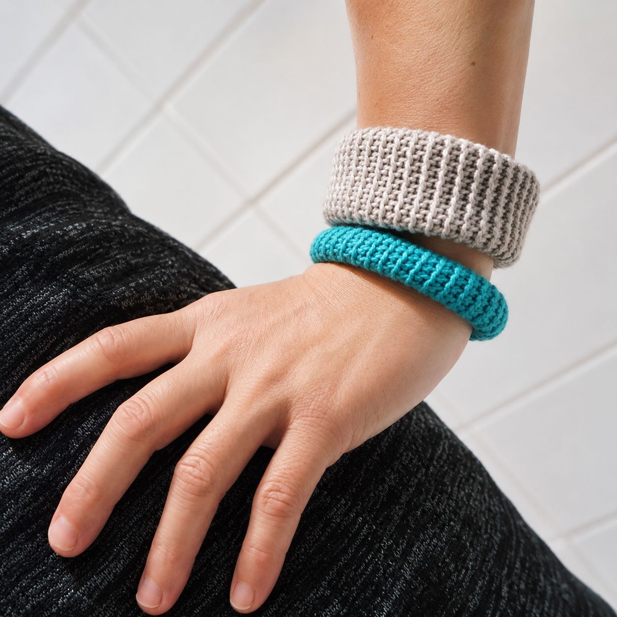 Two gray and teal crochet bangle bracelets with ribbed stitch pattern worn on wrist