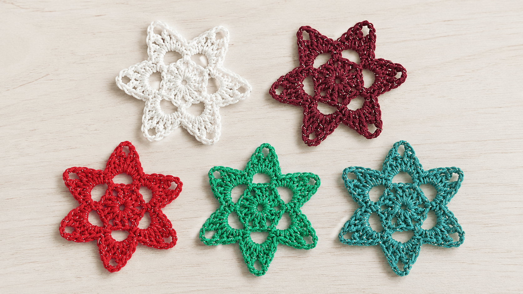 Four handmade crochet star appliques in white, burgundy, red, and teal