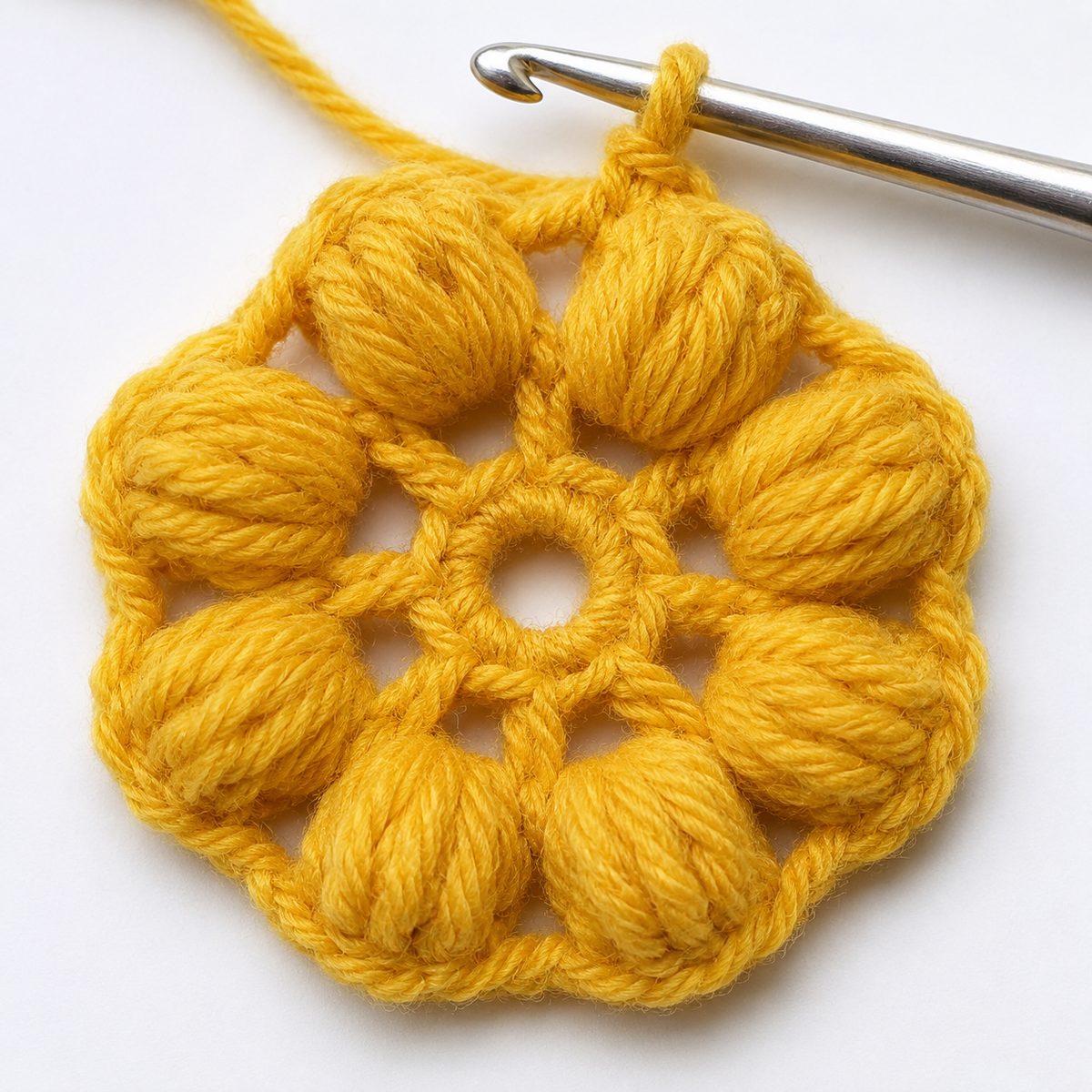 Round 2 of the flower: eight puffy golden yellow bobble stitches around the center ring with the hook mid stitch