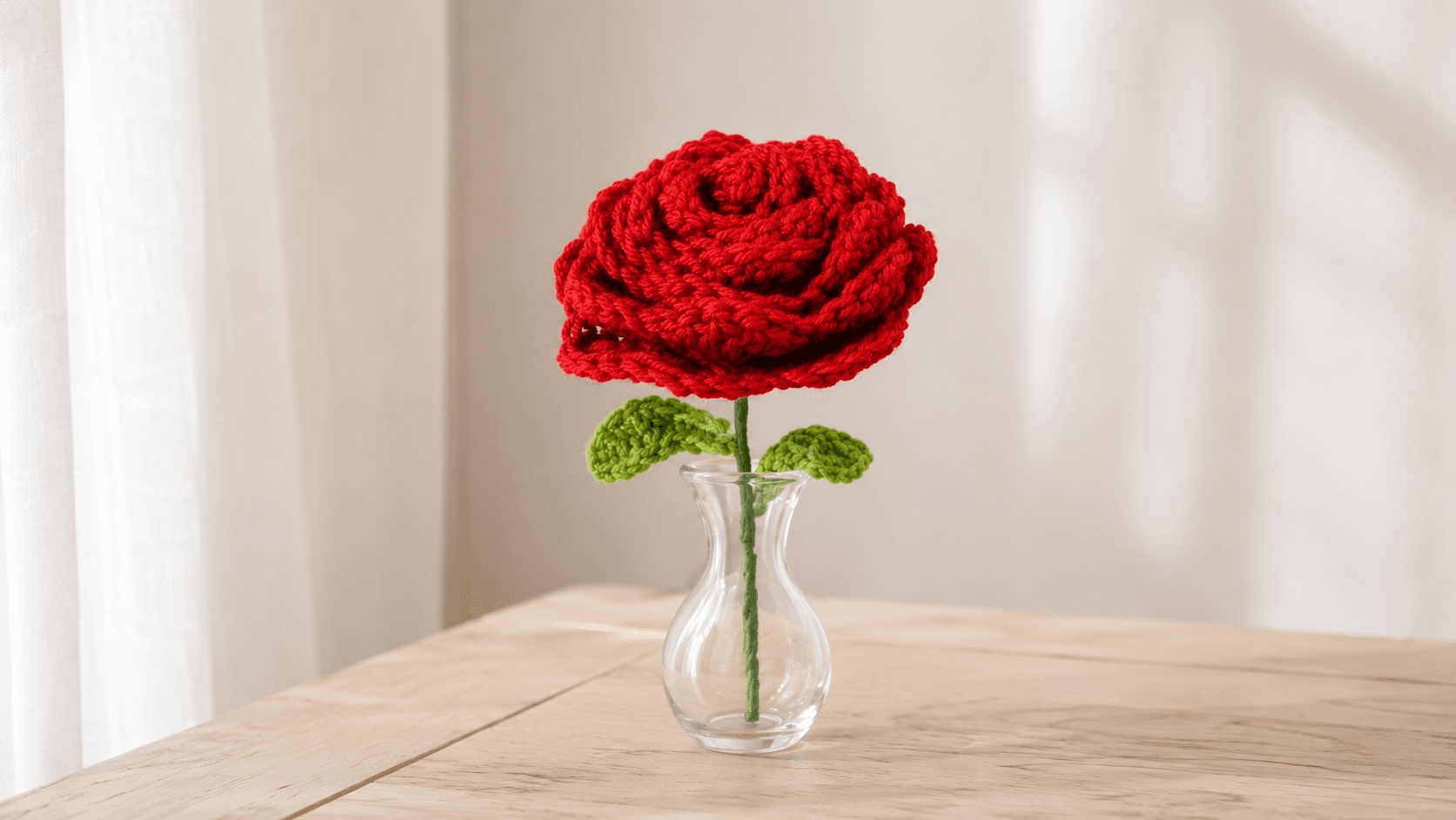 Red handmade crochet rose with green leaves in a glass vase