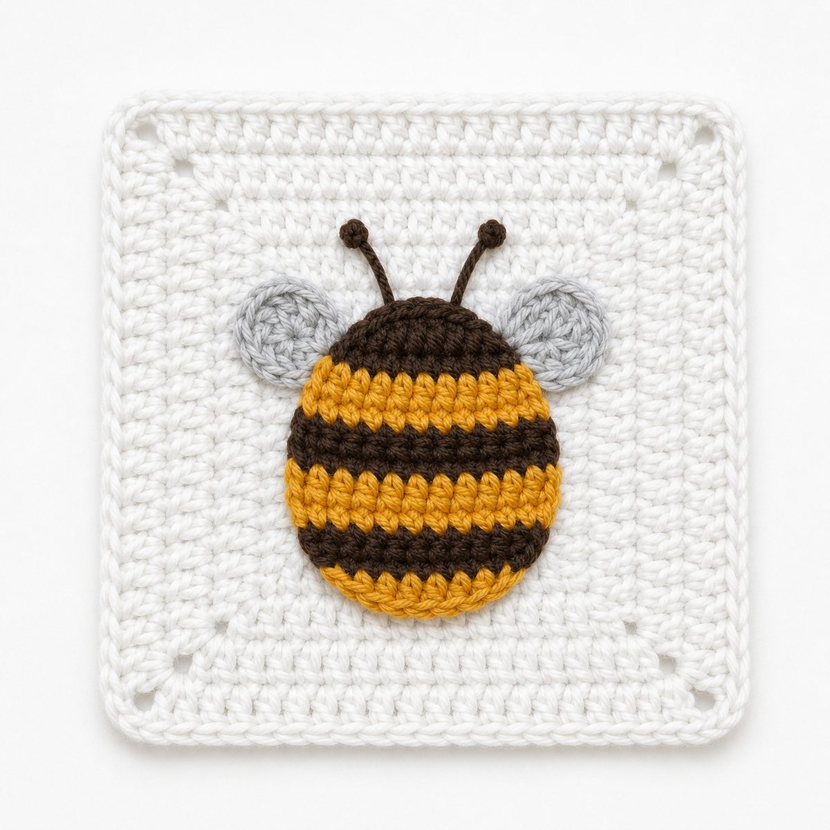 Bee granny square: a flat striped bee in golden yellow and dark brown with pale gray wings and embroidered antennae, set in a solid white crochet square