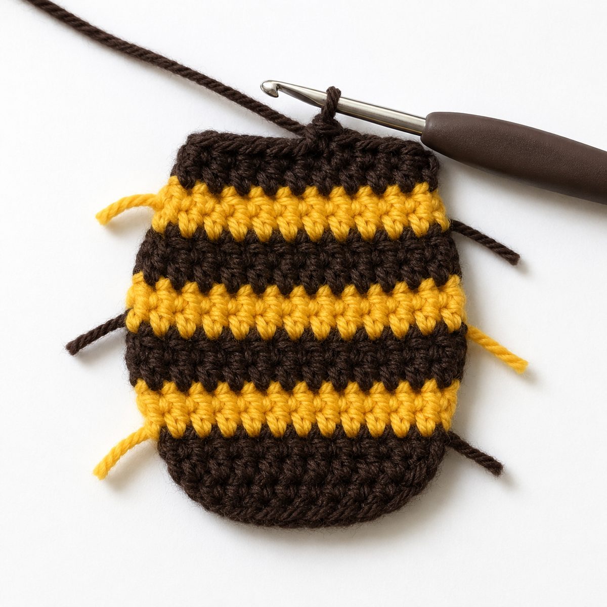 Striped bee body worked flat in golden yellow and dark brown rows with yarn tails at the row ends and a hook at the top