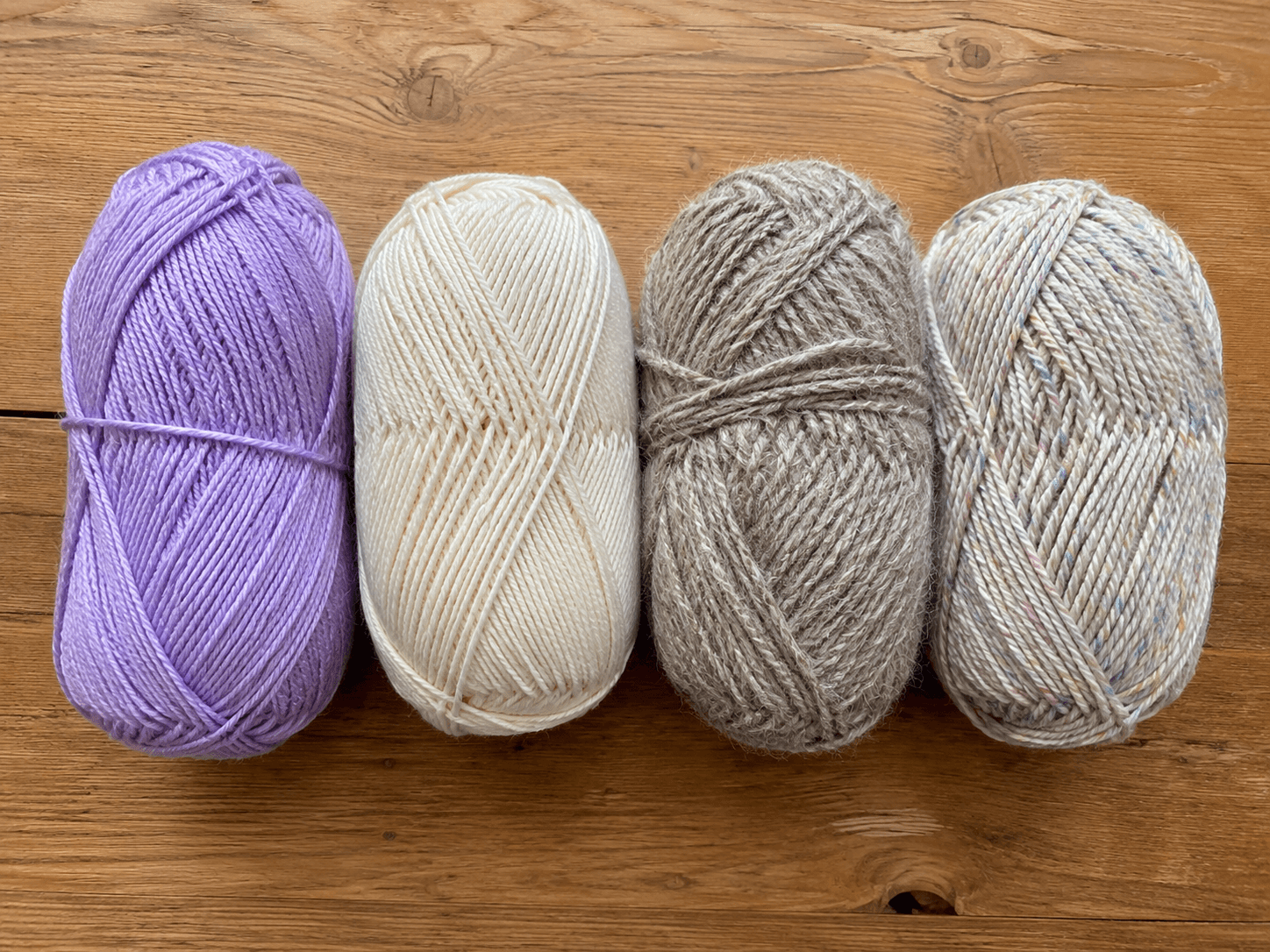 Four balls of yarn in different colors and fiber types side by side