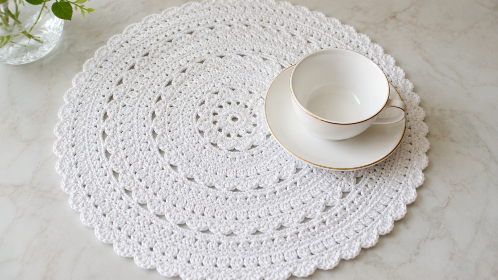 White round lace crochet mat with concentric floral motifs beneath a teacup