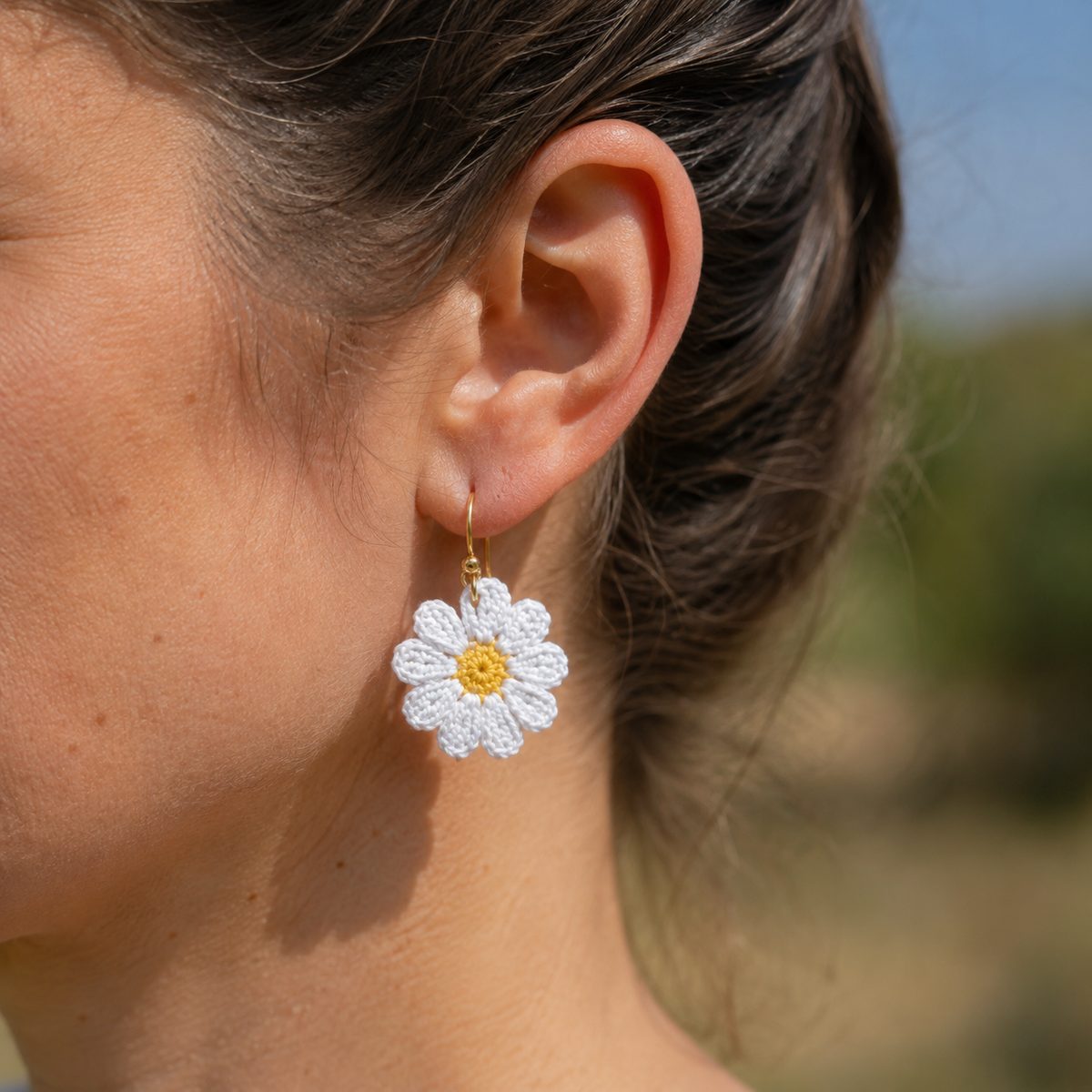 White crochet daisy earring with yellow center worn on the ear in soft outdoor light