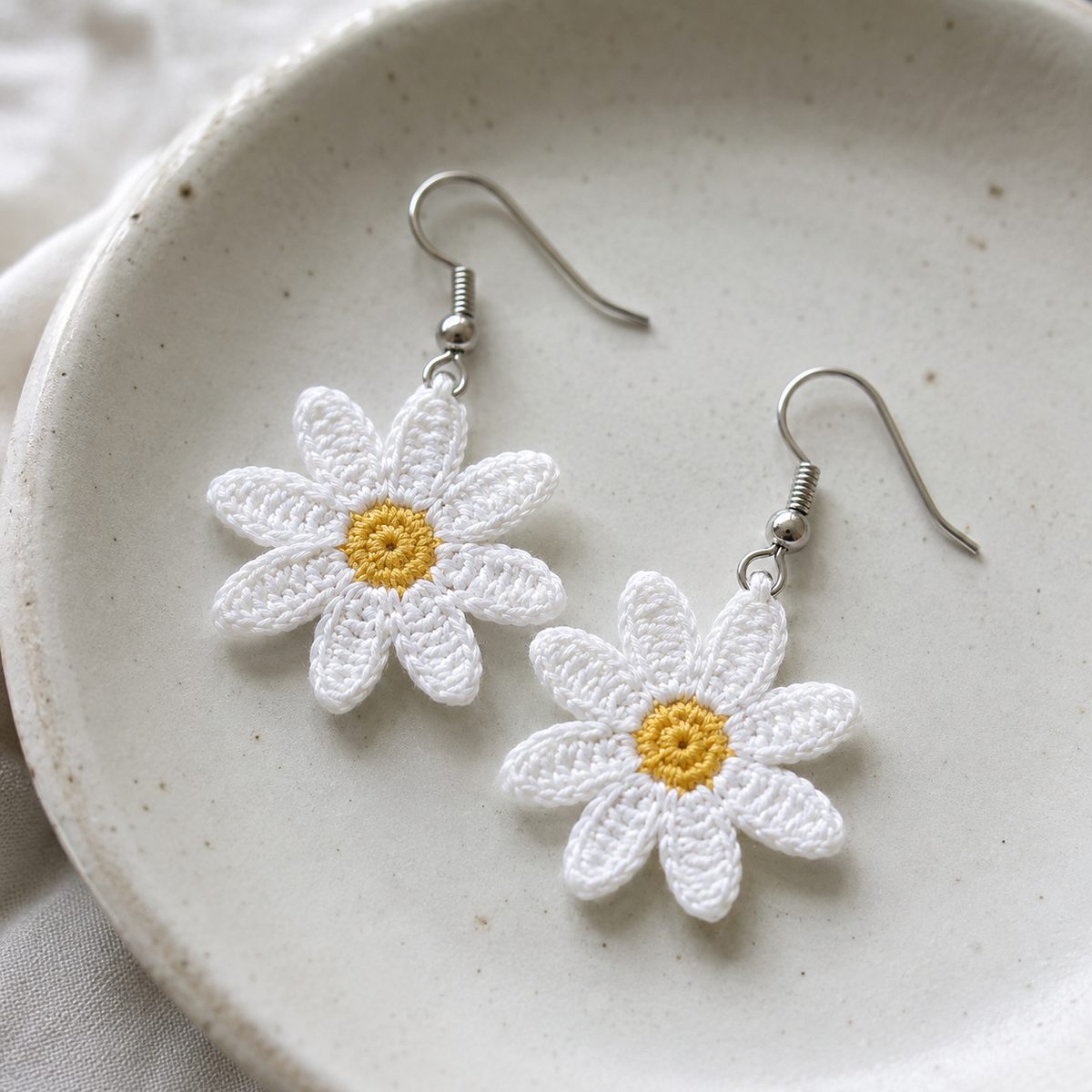 Finished crochet daisy earrings in white thread with yellow centers on a ceramic dish