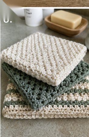 Stack of three handmade crochet cotton dishcloths - cream moss stitch, sage waffle texture and striped - on a kitchen counter beside a soap dish
