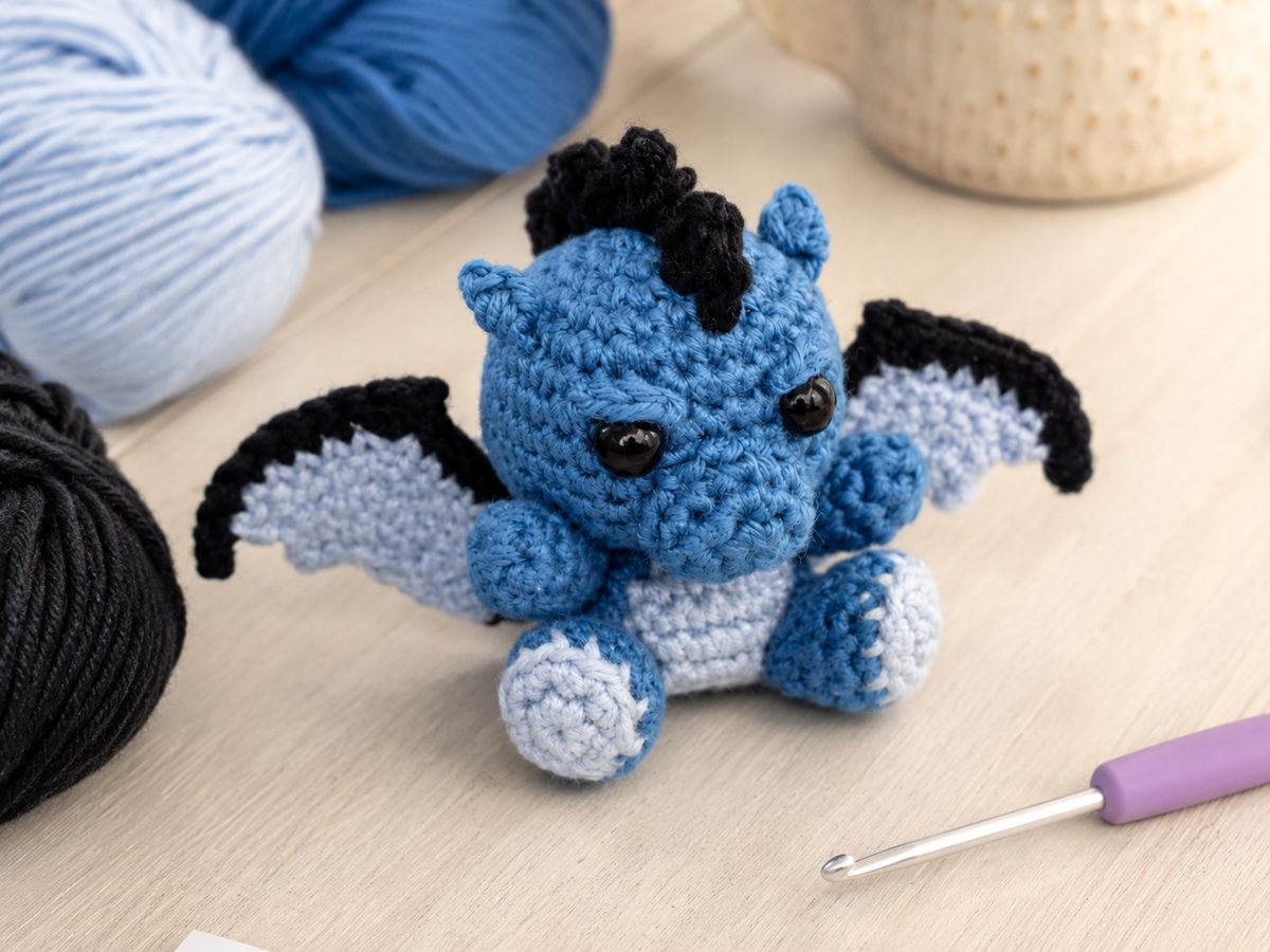 Blue, light blue and black cotton yarn with the finished crochet dragon and a crochet hook