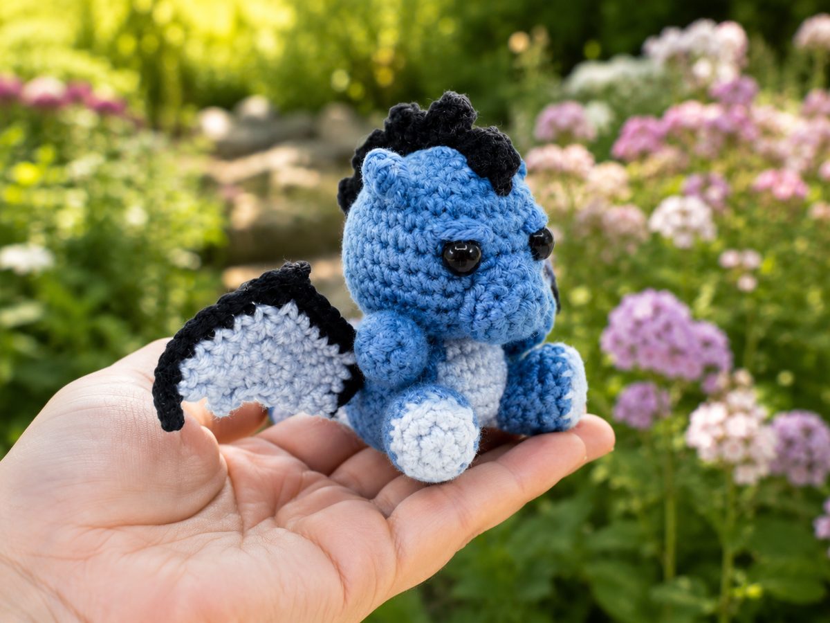 Palm-size blue crochet dragon held in a hand, showing the scalloped two-tone wings