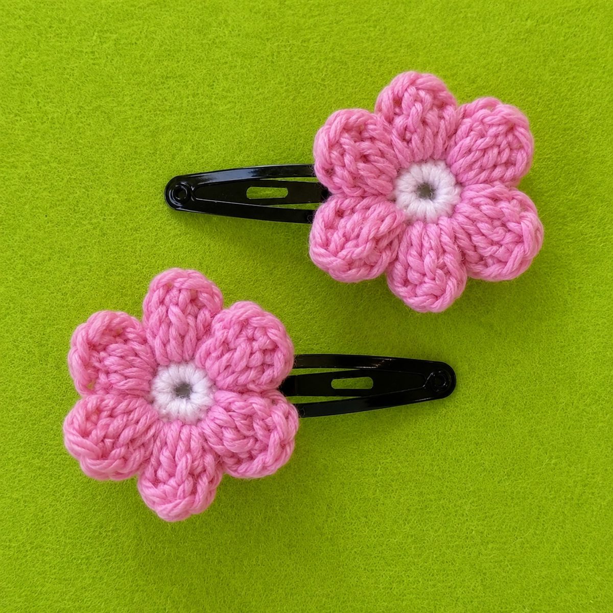 Two pink crochet puff flower hair clips with white centers mounted on black snap clips
