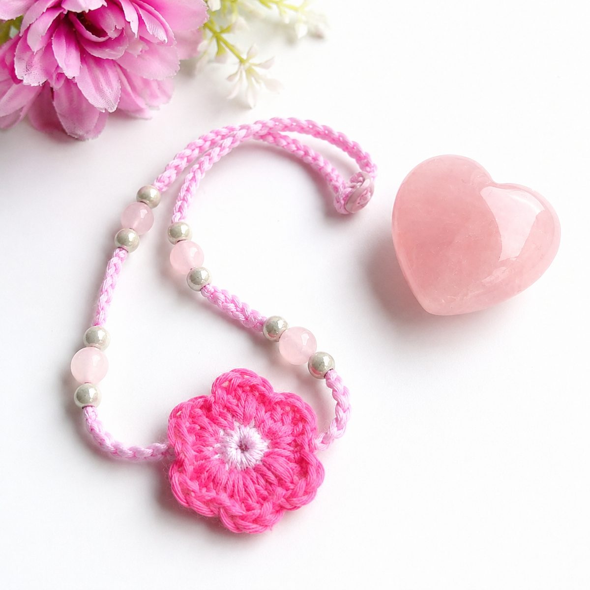 Pink crochet flower necklace on a braided cord with rose quartz beads and a button closure