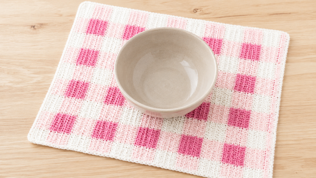 White and pink gingham crochet placemat beneath a beige ceramic bowl