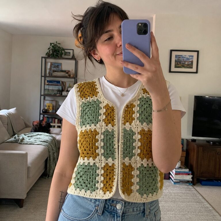 Handmade granny square crochet vest in mustard, sage green and cream squares worn over a white t-shirt, mirror selfie in a real living room