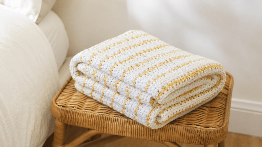 Folded white crochet blanket with mustard yellow stripes and nubby texture