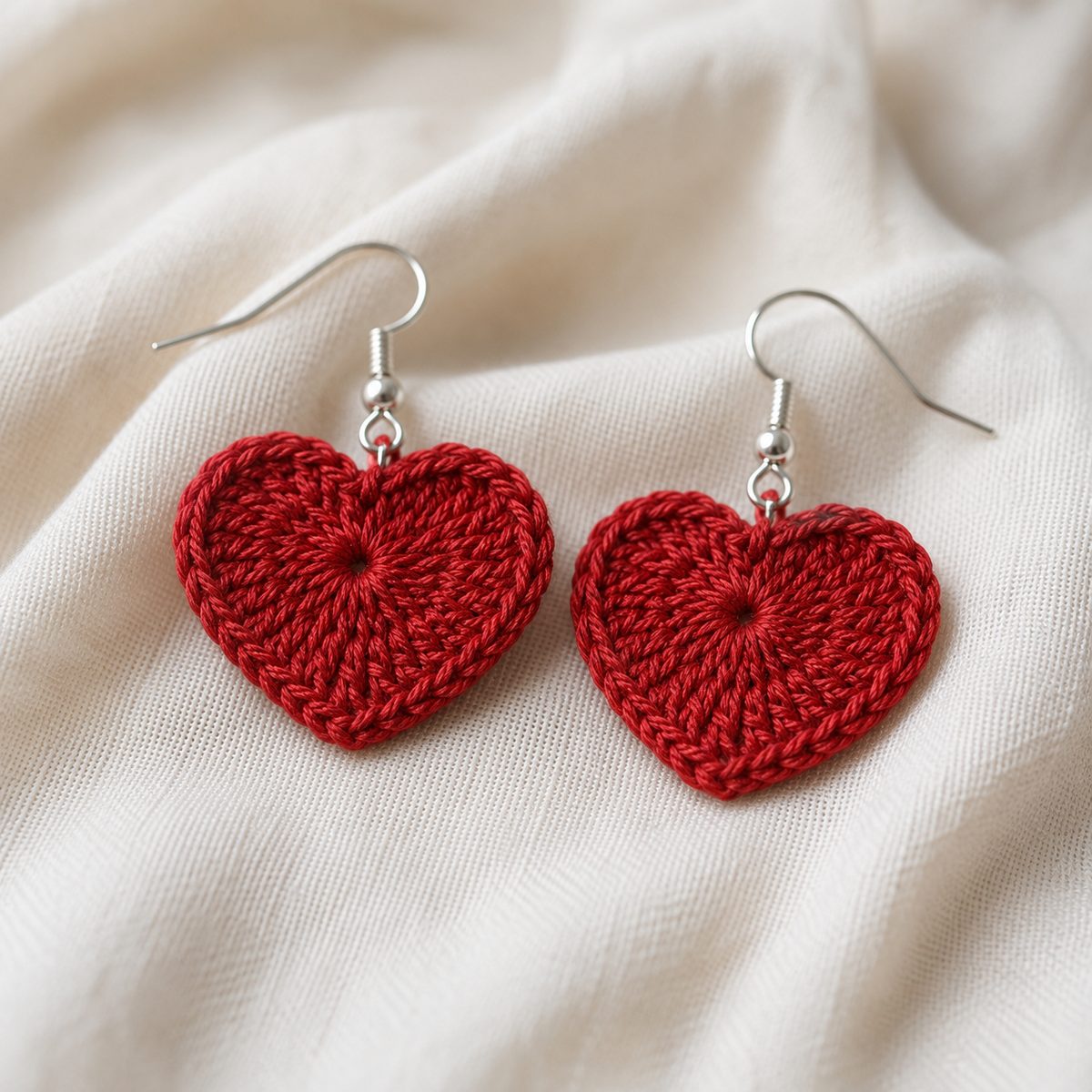 Small red crochet heart earrings in fine cotton thread with silver hooks on cream fabric