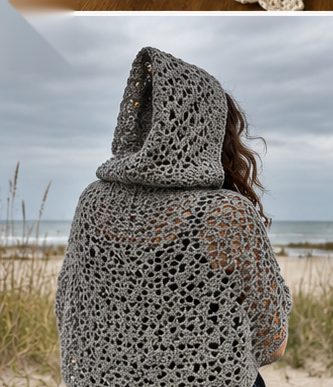 Woman wearing a grey crochet hooded shawl in open lacy stitch seen from behind at a beach on an overcast day