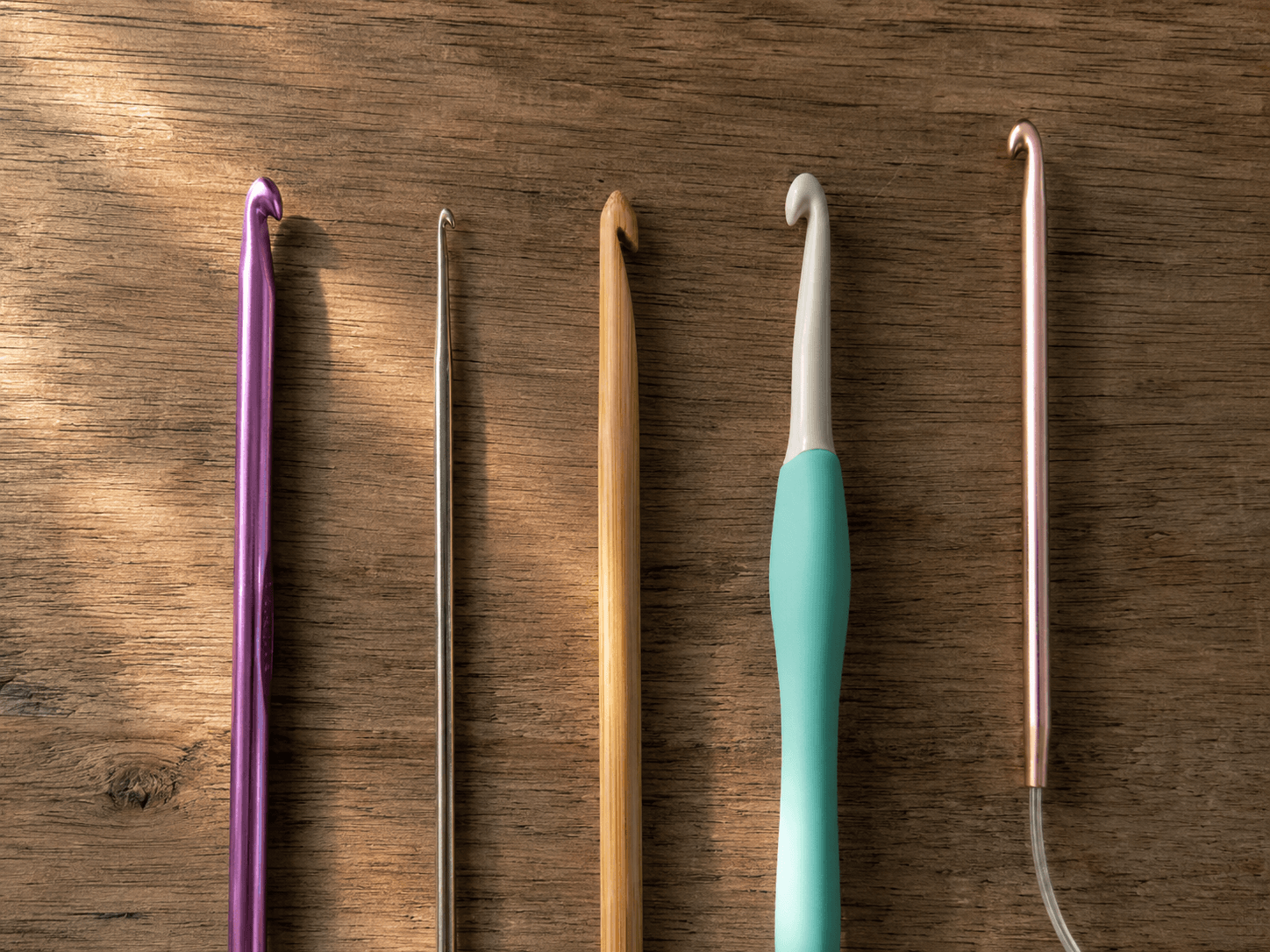 Five crochet hooks side by side: aluminum, steel, bamboo, ergonomic, and Tunisian