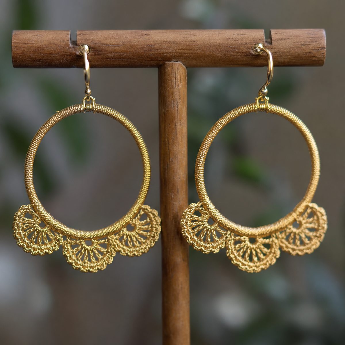 Gold crochet hoop earrings with three lace fans along the bottom curve on a wooden stand