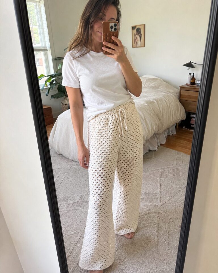 Mirror selfie of a woman wearing handmade cream crochet lounge pants with a drawstring waist and granny stitch fabric, worn with a plain white t-shirt in a real bedroom