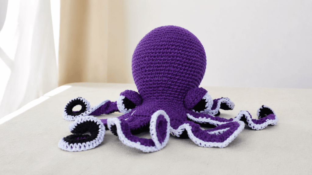 Purple crocheted octopus with curled tentacles and contrasting underside