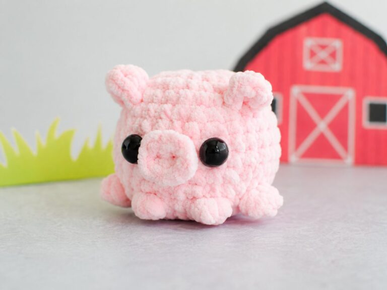 Crochet pig pattern finished, pink chenille pocket pig with spiral snout and safety eyes in front of a toy barn