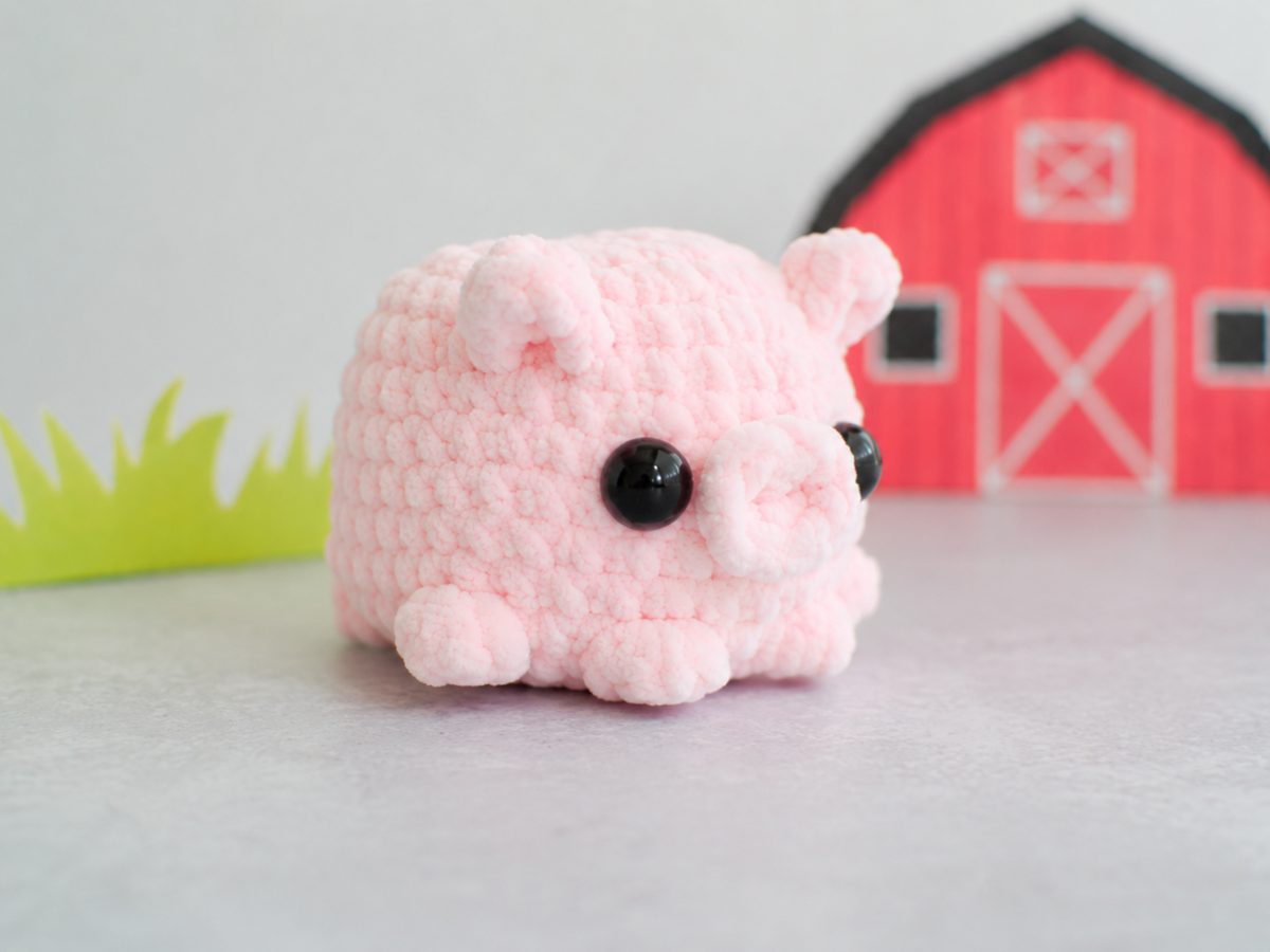 Side view of the pink crochet pig showing the folded ears and four popcorn feet at the base