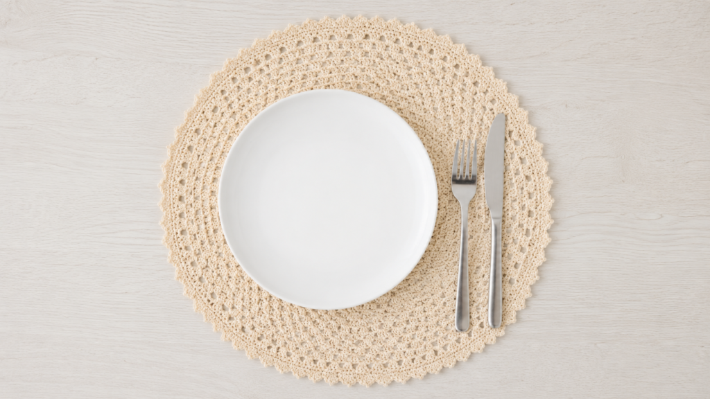 Ivory round openwork crochet placemat with a scalloped edge beneath a white plate