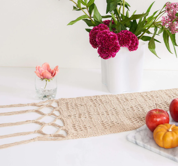 Beige filet crochet table runner with braided fringe on a white table
