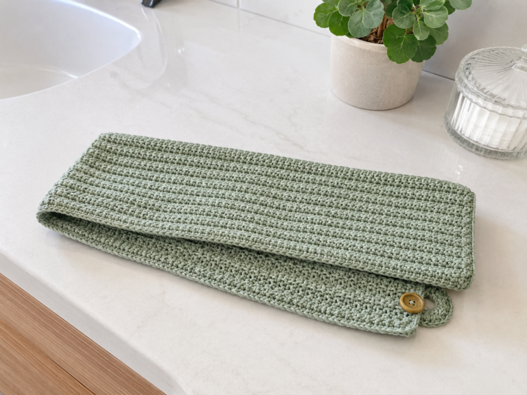 Folded sage green ribbed crochet hair towel with wood button on a bathroom counter