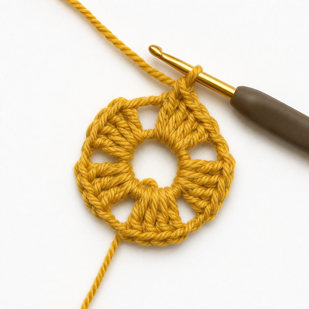 Start of the hexagon: golden yellow double crochet groups with chain gaps worked around the center ring, hook mid stitch