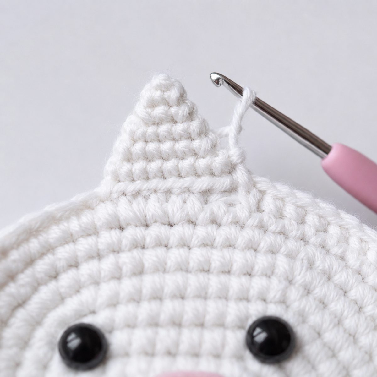 Small white triangle ear crocheted in rows on the edge of the kitten face, hook in the loop
