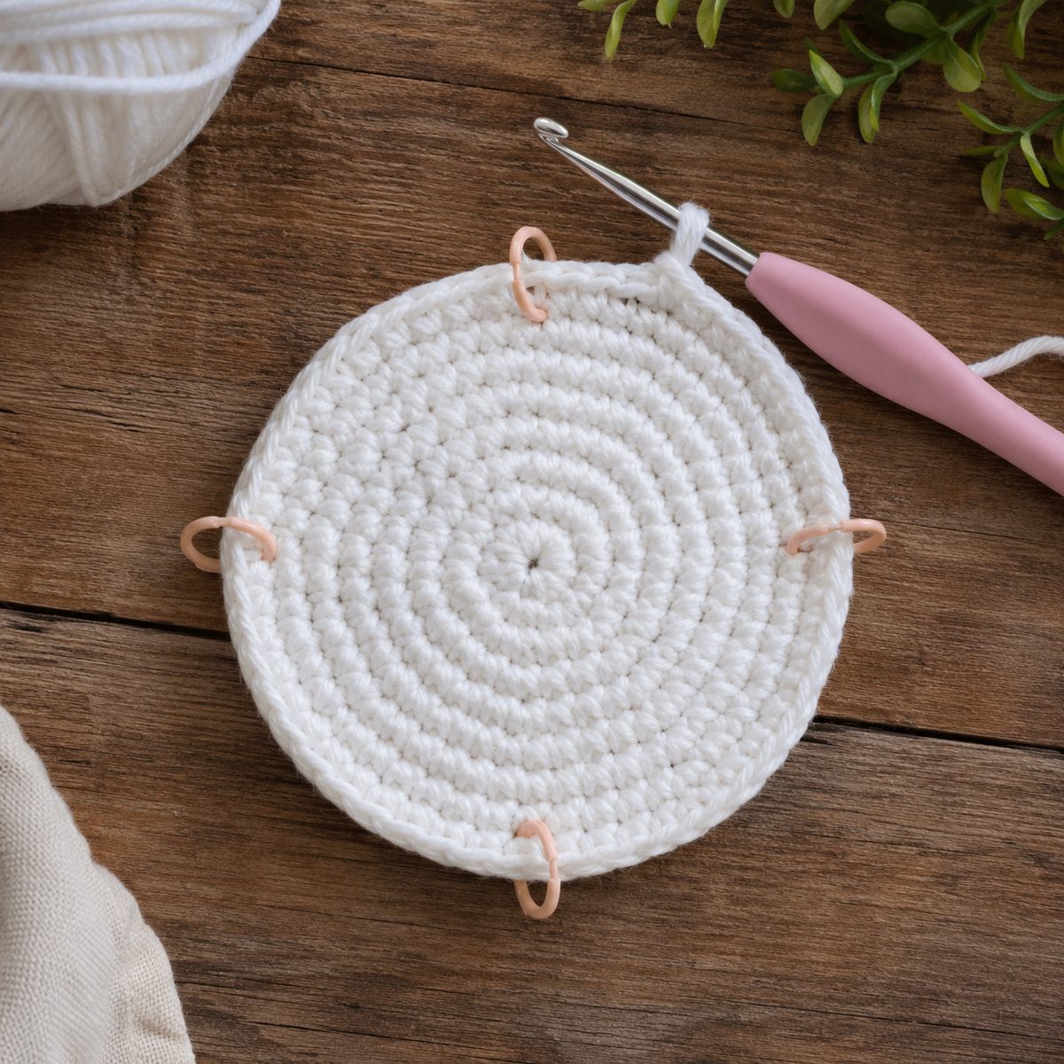 White single crochet circle with four stitch markers placed for the square corners, hook attached