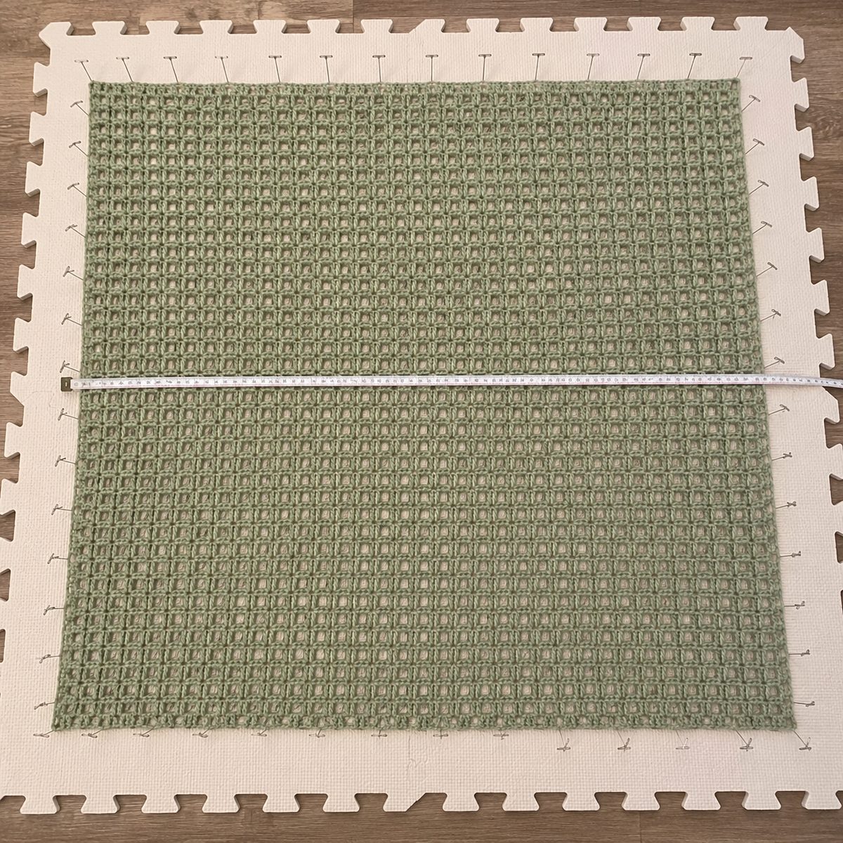 One rectangular mesh panel wet blocked and pinned square on a foam mat with a measuring tape across its width