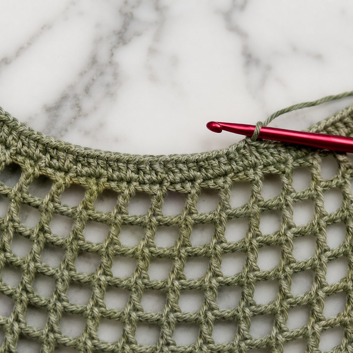 Red hook working a round of single crochet edging along the curved neckline of the sage green mesh top