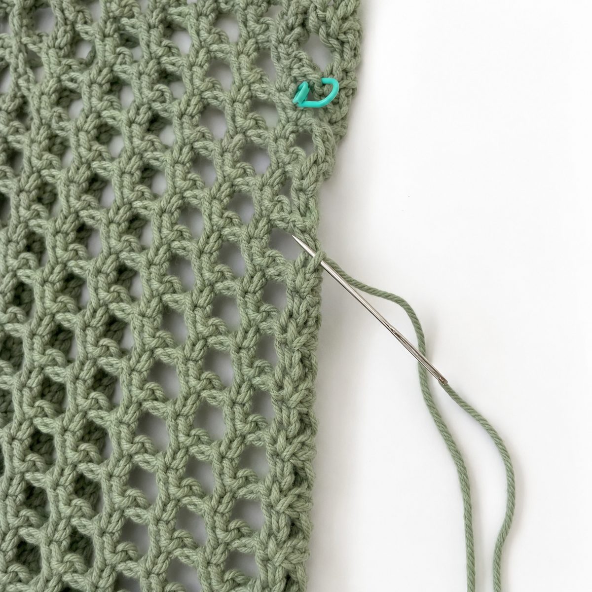 Yarn needle whip stitching the side seam of the mesh top with a stitch marker holding the armhole opening
