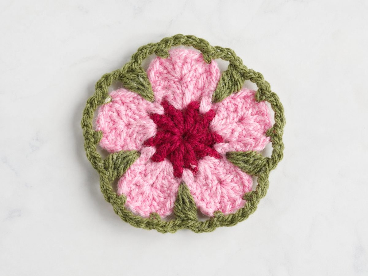 Petal granny square flower center: five pale pink picot petals around a raspberry wheel, framed by a leaf green bobble halo